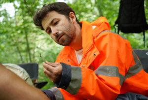 Un technicien observe un invertébré prélevé à l'aide d'une pince à épiler dans le tamis.