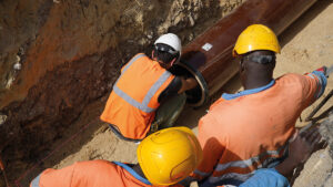 Trois hommes de chantier dans une tranchée. Un ouvrier ajuste la pose d'une canalisation neuve d'assainissement.